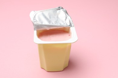 Photo of Delicious yogurt in plastic cup on light pink background, closeup