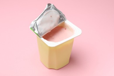 Photo of Delicious yogurt in plastic cup on light pink background, closeup