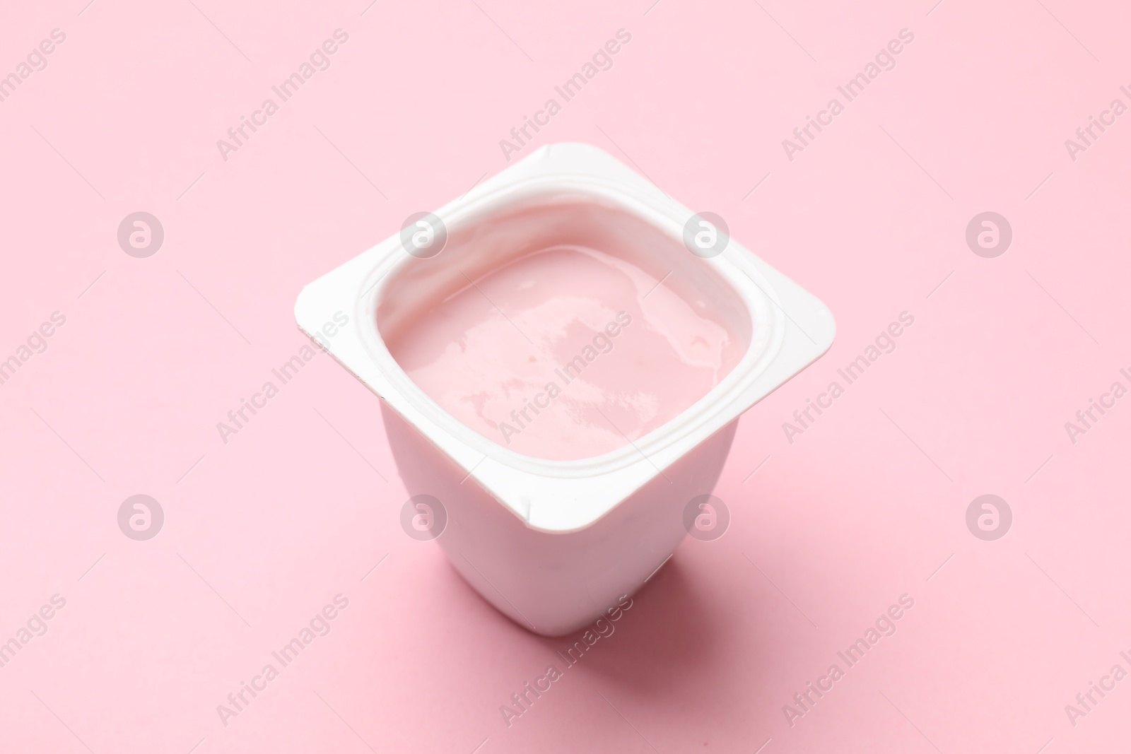 Photo of Delicious yogurt in plastic cup on light pink background, closeup