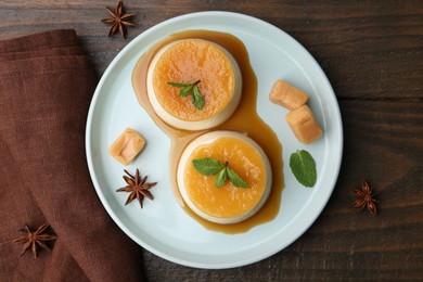 Photo of Tasty puddings with caramel sauce served on wooden table, flat lay