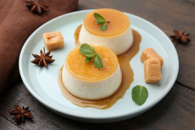 Tasty puddings with caramel sauce served on wooden table, closeup