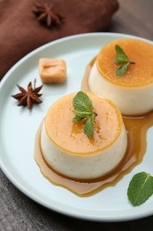 Photo of Tasty puddings with caramel sauce served on wooden table, closeup