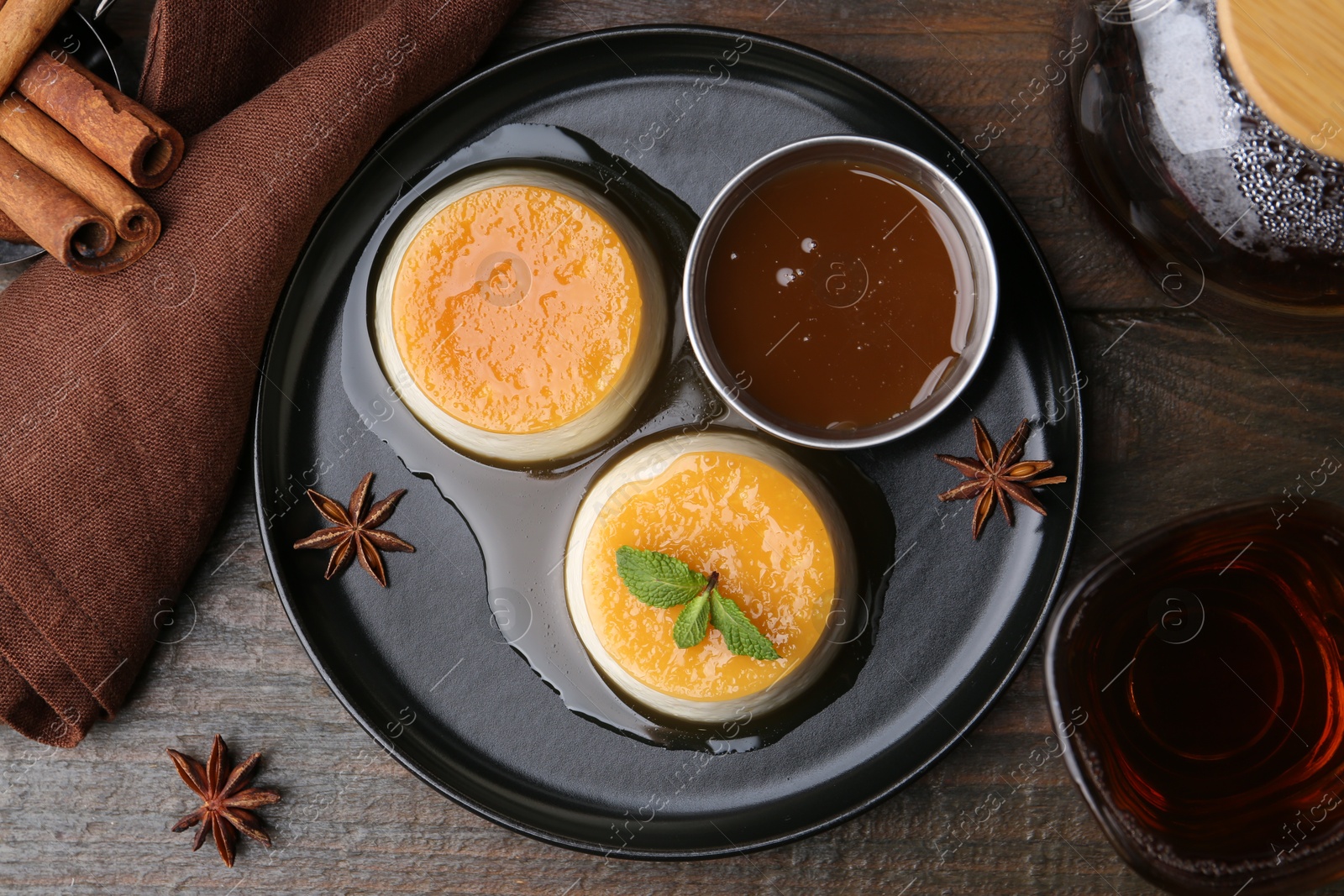 Photo of Tasty puddings with caramel sauce served on wooden table, flat lay