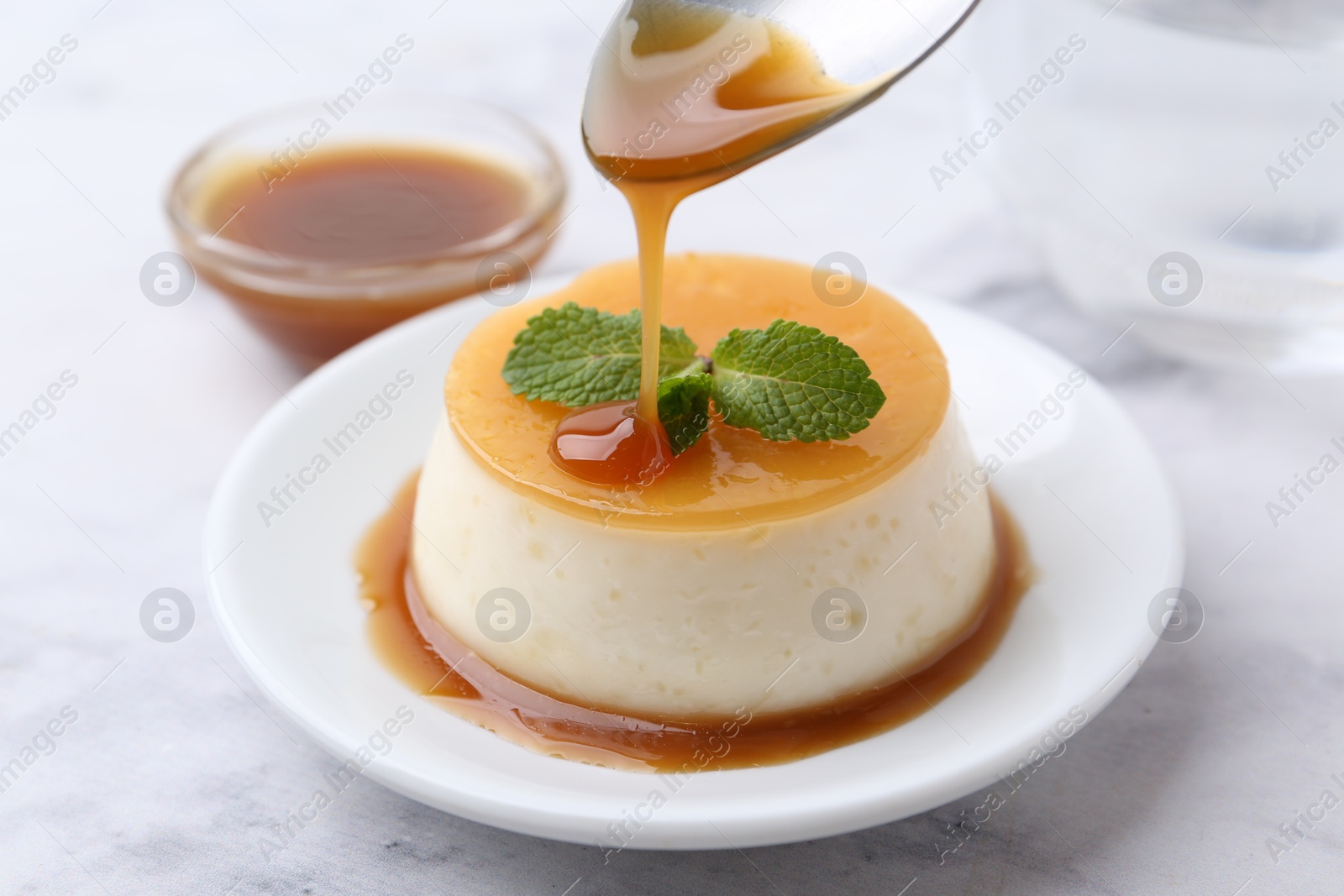 Photo of Tasty pudding with caramel sauce served on white marble table, closeup