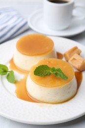 Photo of Tasty puddings with caramel sauce served on white tiled table, closeup