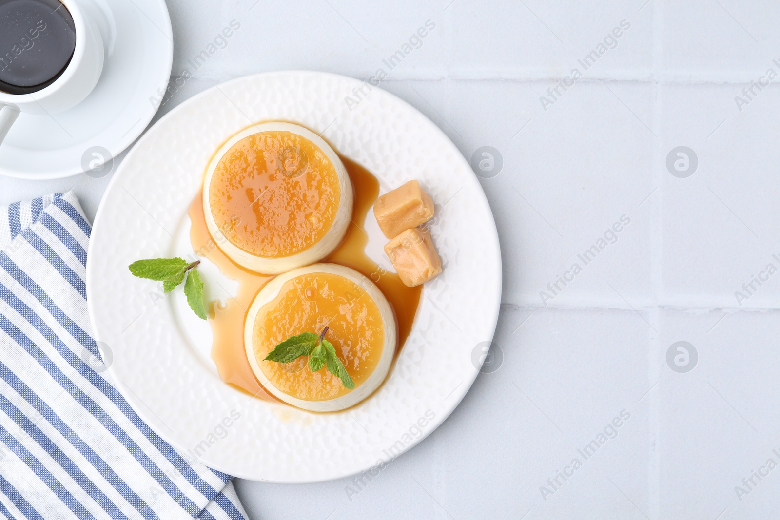 Photo of Tasty puddings with caramel sauce served on white tiled table, top view. Space for text