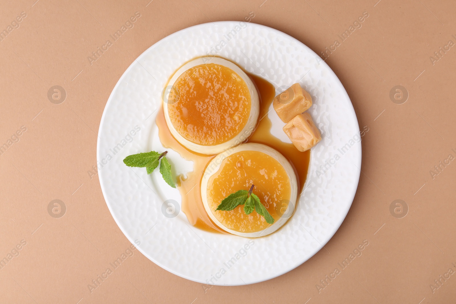 Photo of Tasty puddings with caramel sauce served on light brown background, top view