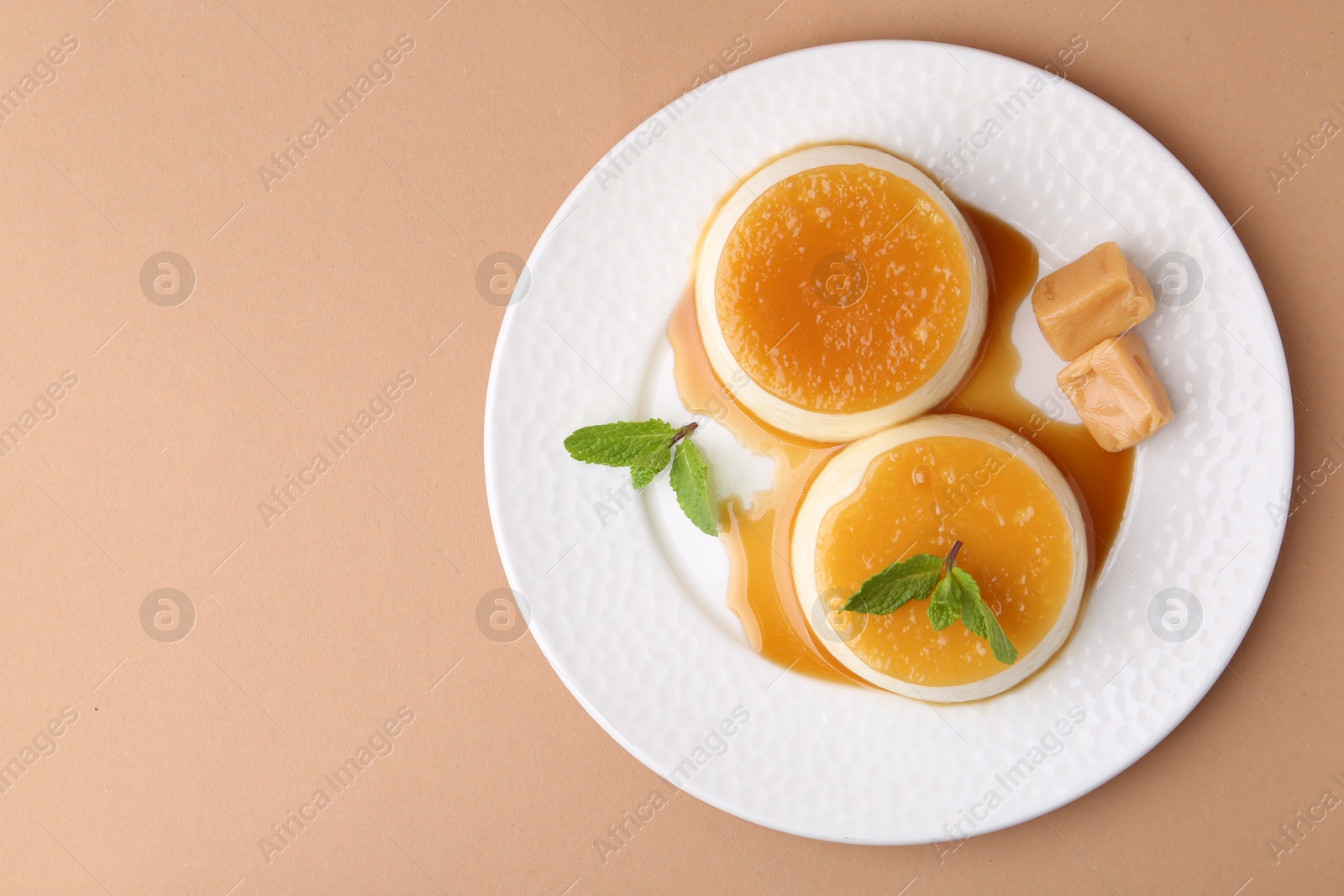 Photo of Tasty puddings with caramel sauce served on light brown background, top view. Space for text