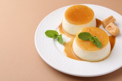 Photo of Tasty puddings with caramel sauce served on light brown background, closeup. Space for text