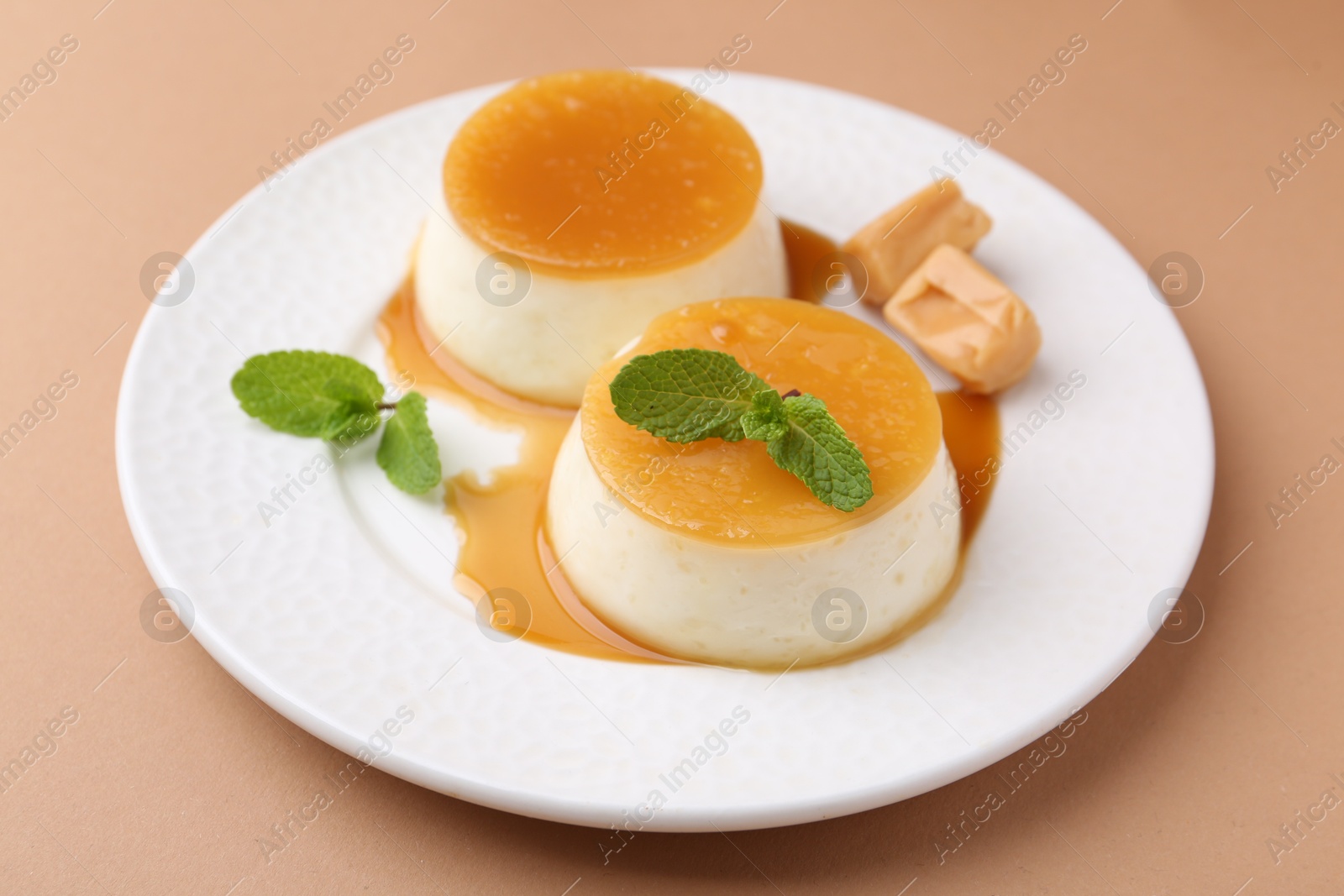 Photo of Tasty puddings with caramel sauce served on light brown background, closeup