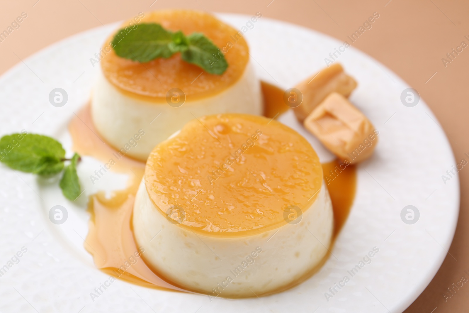 Photo of Tasty puddings with caramel sauce served on light brown background, closeup