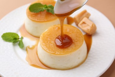 Photo of Pouring caramel sauce onto tasty pudding on light brown background, closeup