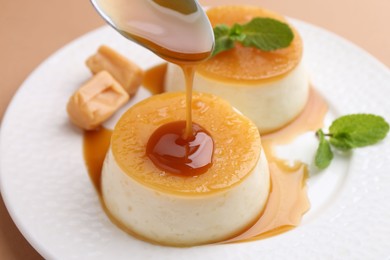 Photo of Pouring caramel sauce onto tasty pudding on light brown background, closeup