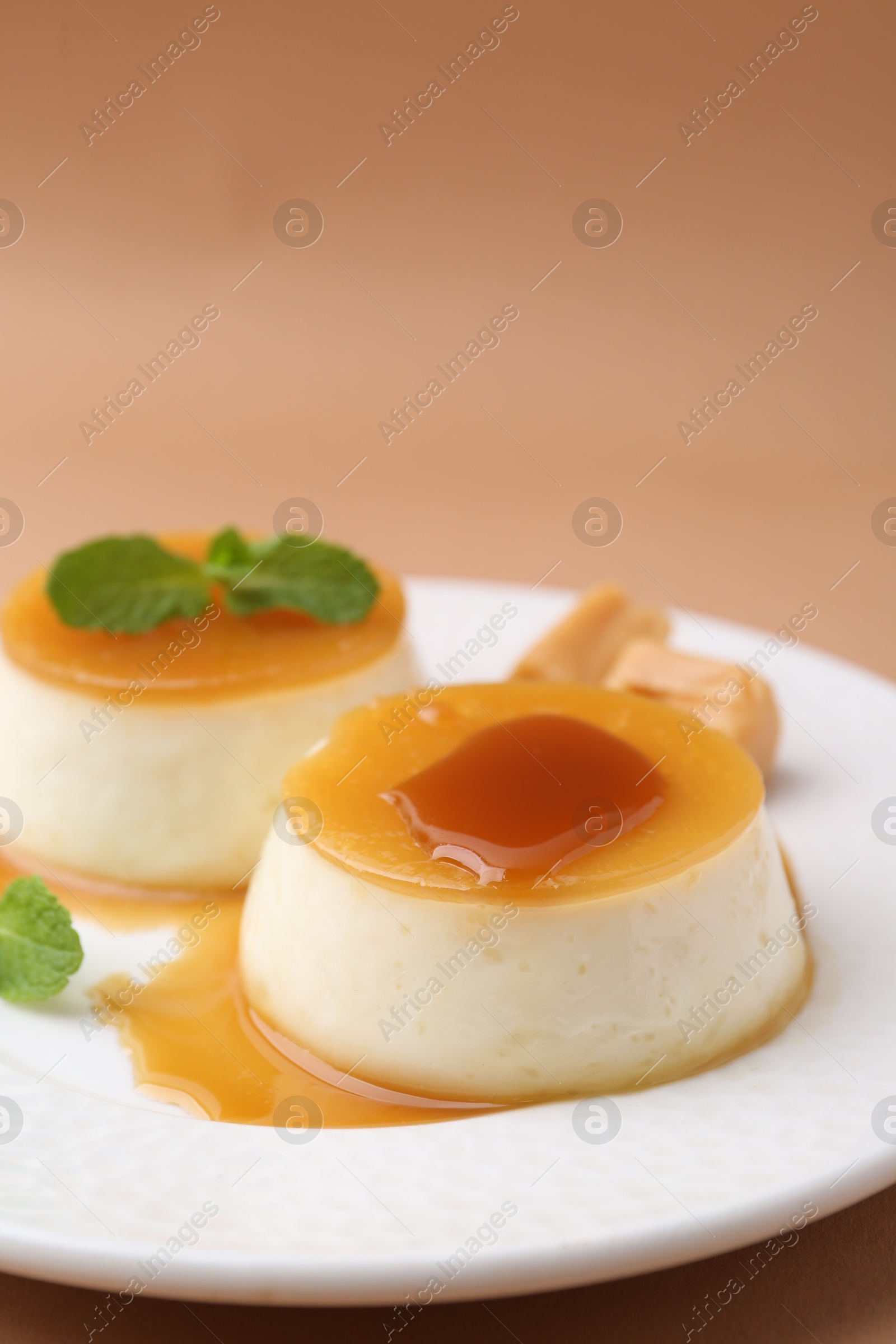 Photo of Tasty puddings with caramel sauce served on light brown background, closeup