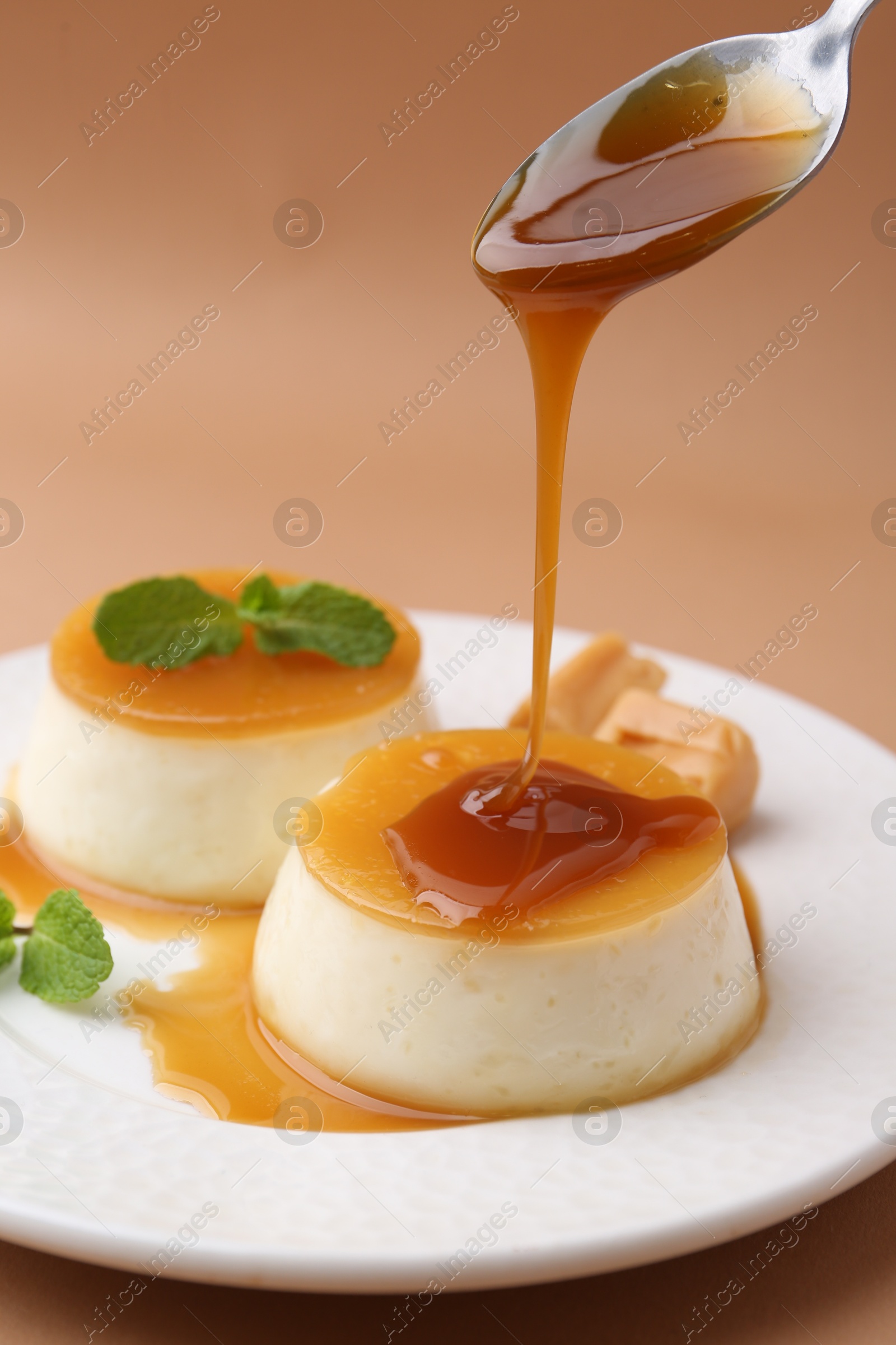 Photo of Pouring caramel sauce onto tasty pudding on light brown background, closeup