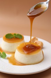 Photo of Pouring caramel sauce onto tasty pudding on light brown background, closeup