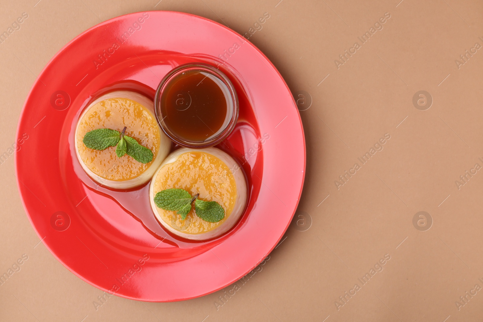 Photo of Tasty puddings with caramel sauce served on light brown background, top view. Space for text