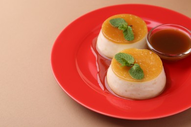 Photo of Tasty puddings with caramel sauce served on light brown background, closeup. Space for text