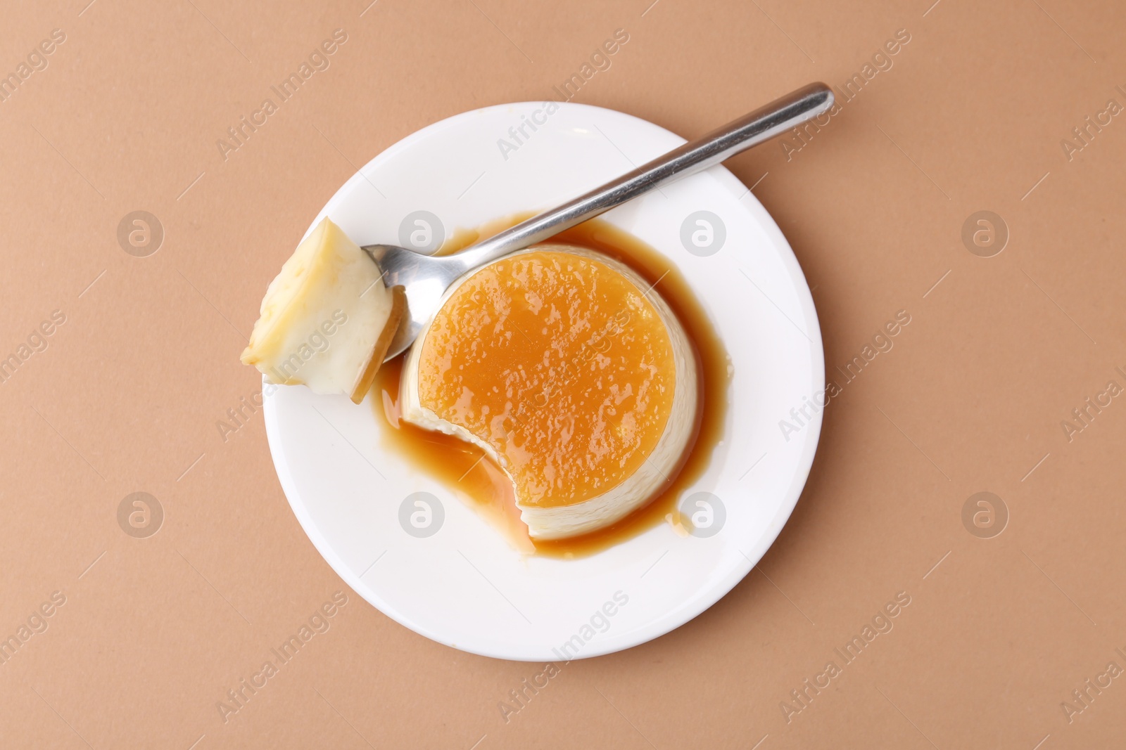 Photo of Tasty pudding with caramel sauce served on light brown background, top view