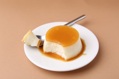 Photo of Tasty pudding with caramel sauce served on light brown background, closeup