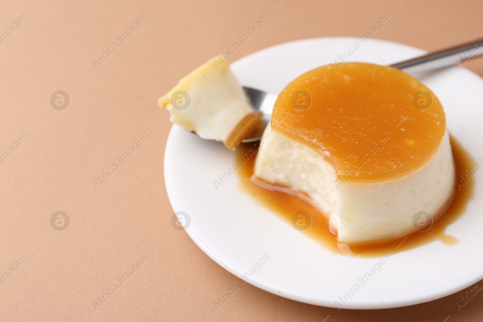 Photo of Tasty pudding with caramel sauce served on light brown background, closeup. Space for text