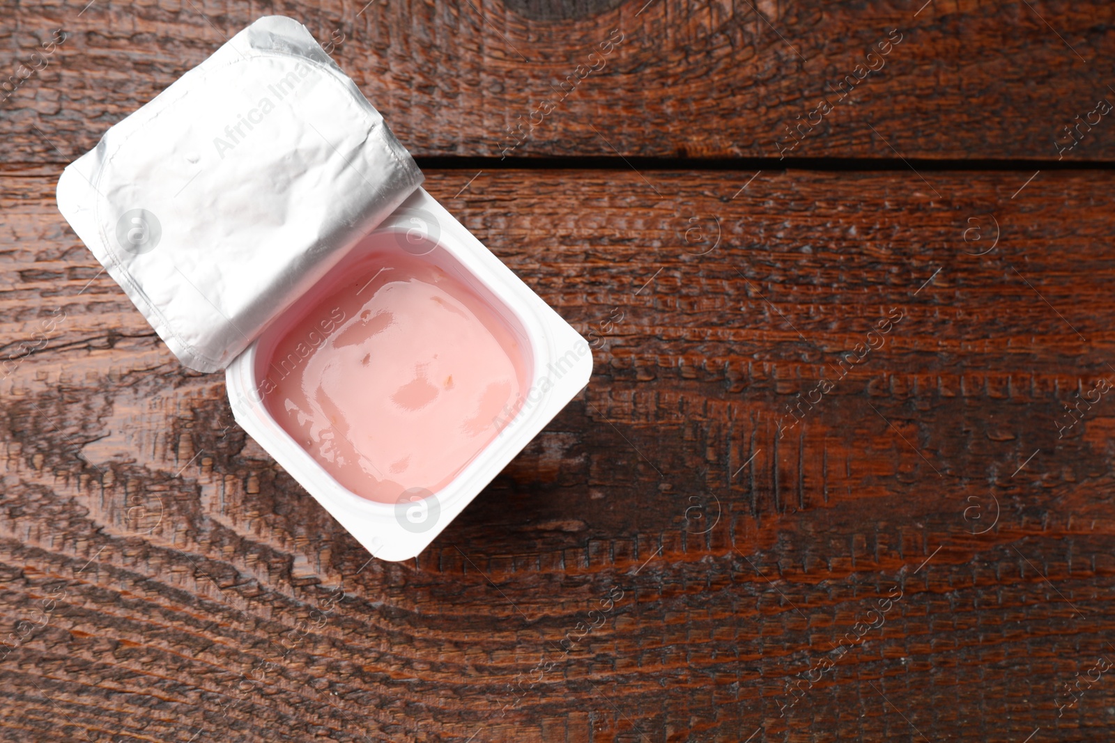 Photo of Delicious yogurt in plastic cup on wooden table, top view. Space for text