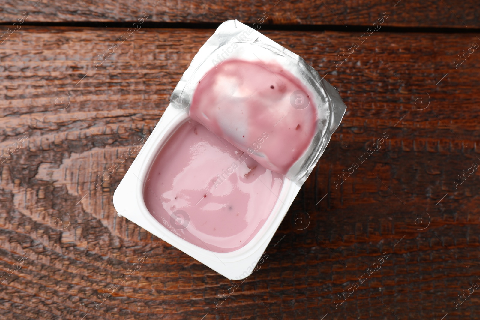 Photo of Delicious yogurt in plastic cup with spoon on wooden table, top view