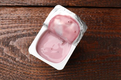 Photo of Delicious yogurt in plastic cup with spoon on wooden table, top view