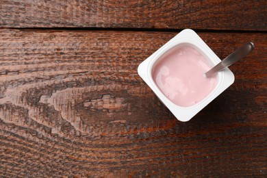 Photo of Delicious yogurt in plastic cup with spoon on wooden table, top view. Space for text