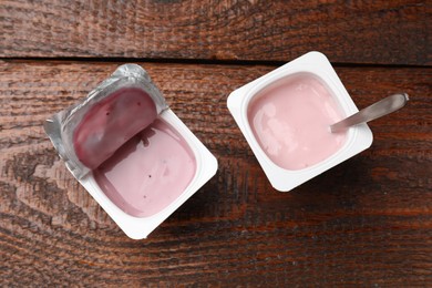 Photo of Delicious yogurts in plastic cups on wooden table, flat lay