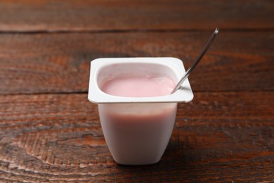 Photo of Delicious yogurt in plastic cup with spoon on wooden table, closeup