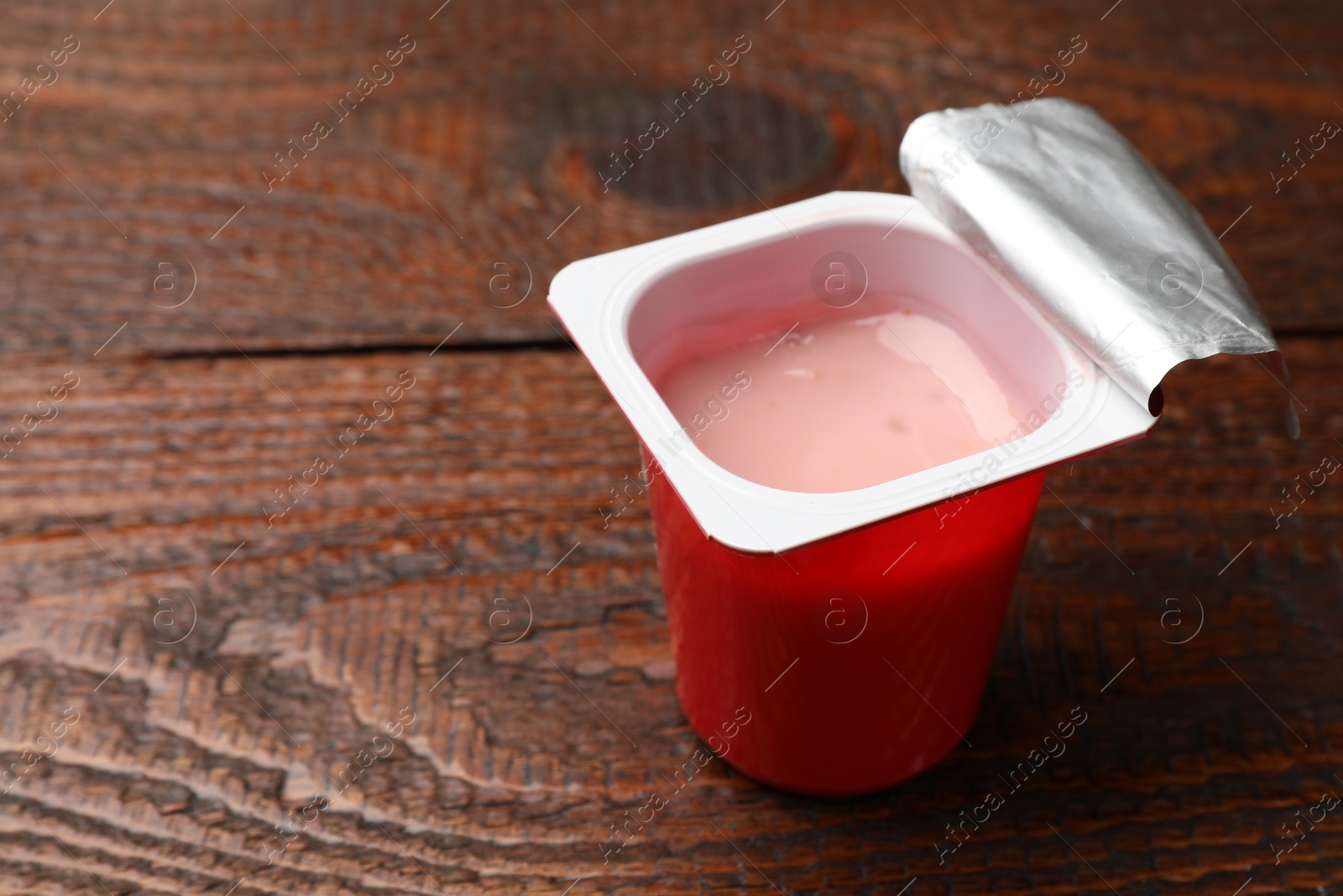 Photo of Delicious yogurt in plastic cup on wooden table, closeup. Space for text