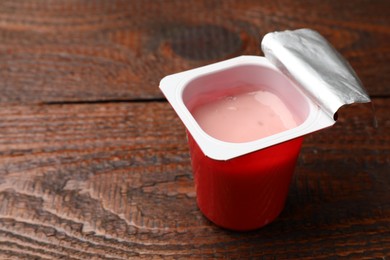 Photo of Delicious yogurt in plastic cup on wooden table, closeup. Space for text