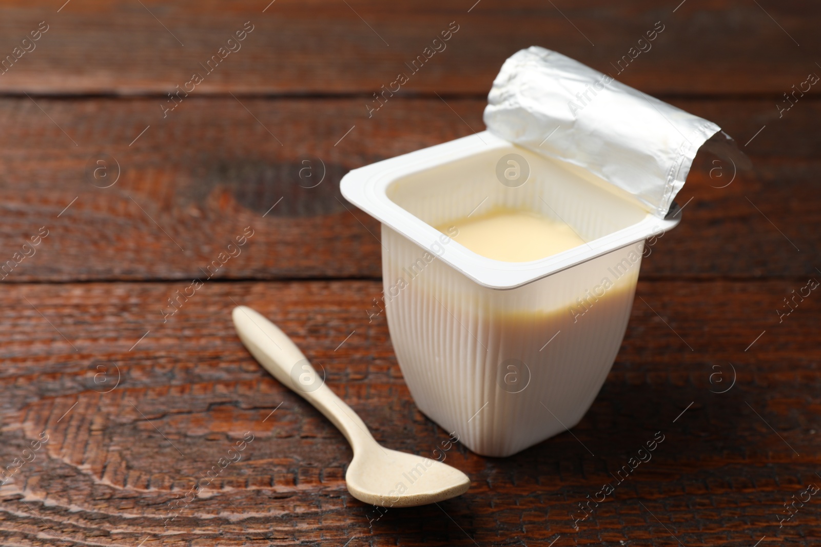 Photo of Delicious yogurt in plastic cup with spoon on wooden table, closeup. Space for text