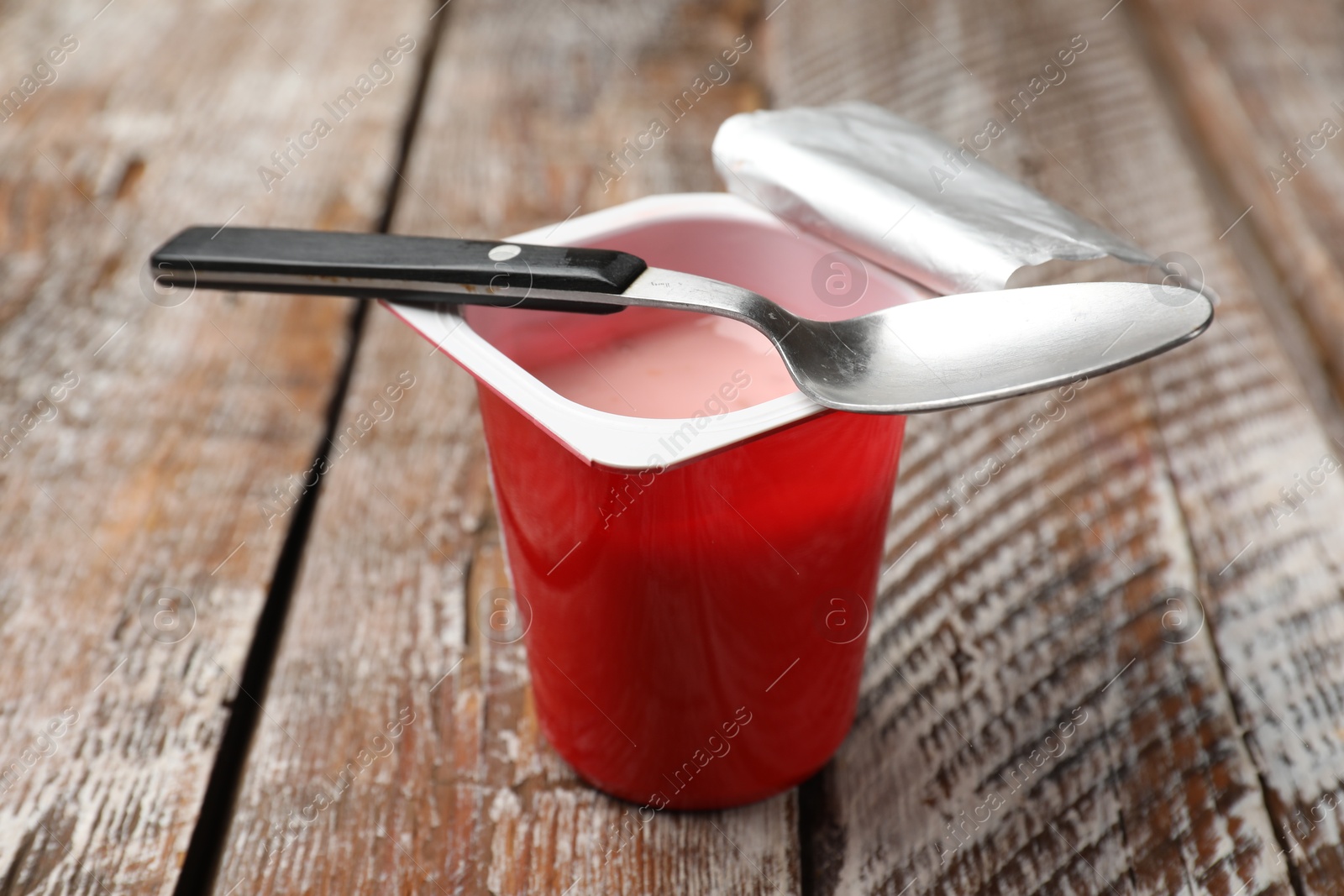 Photo of Delicious yogurt in plastic cup with spoon on wooden table, closeup