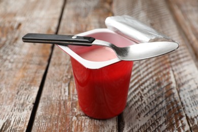 Photo of Delicious yogurt in plastic cup with spoon on wooden table, closeup