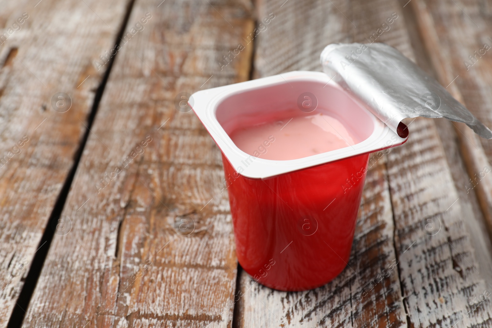 Photo of Delicious yogurt in plastic cup on wooden table, closeup. Space for text