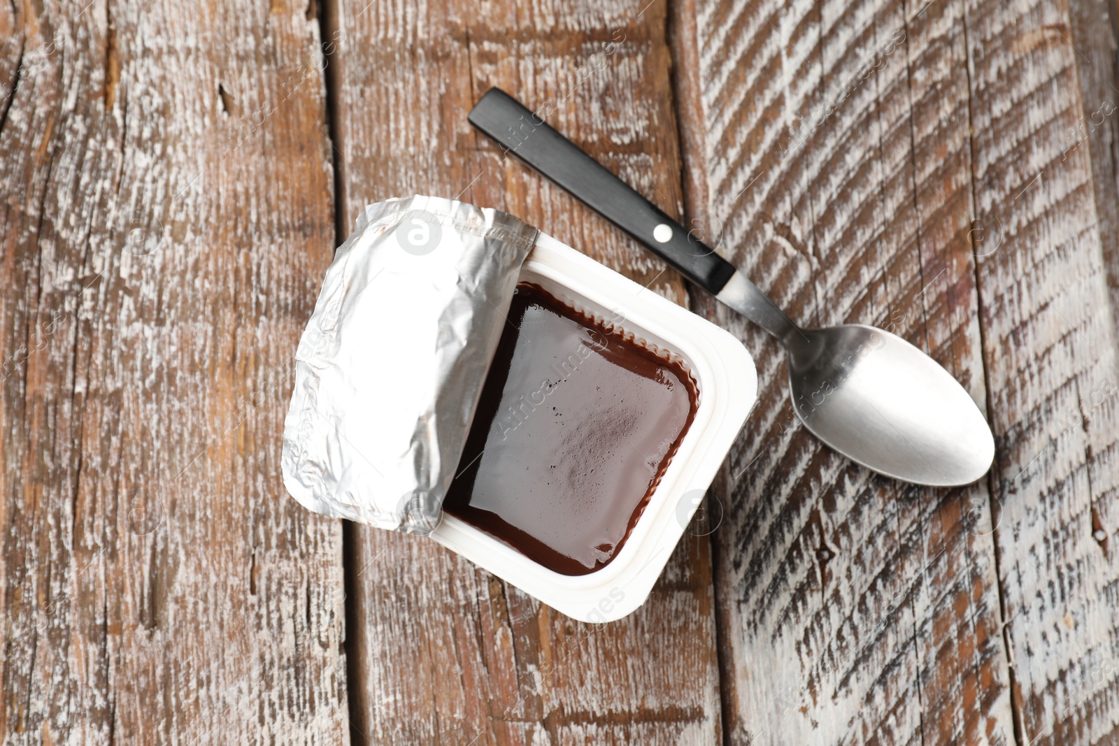 Photo of Delicious chocolate yogurt in plastic cup with spoon on wooden table, flat lay