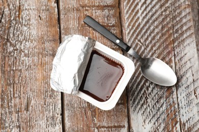 Photo of Delicious chocolate yogurt in plastic cup with spoon on wooden table, flat lay