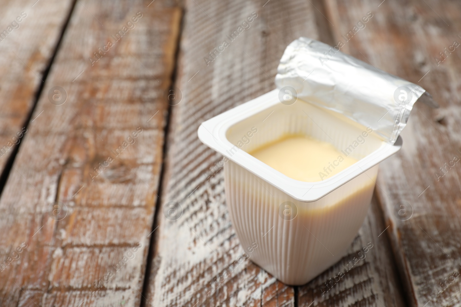 Photo of Delicious yogurt in plastic cup on wooden table, closeup. Space for text