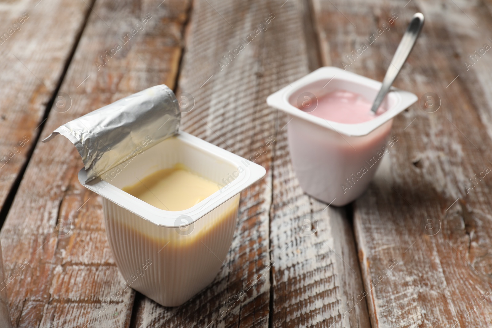 Photo of Delicious yogurts in plastic cups on wooden table, closeup