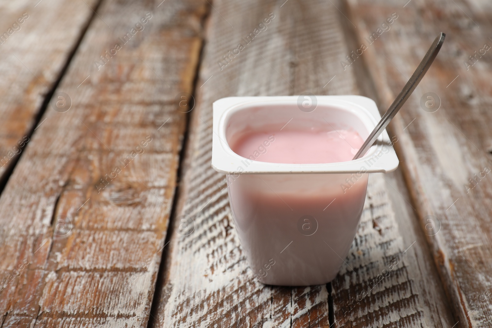 Photo of Delicious yogurt in plastic cup with spoon on wooden table, closeup. Space for text