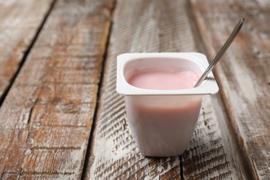 Photo of Delicious yogurt in plastic cup with spoon on wooden table, closeup. Space for text