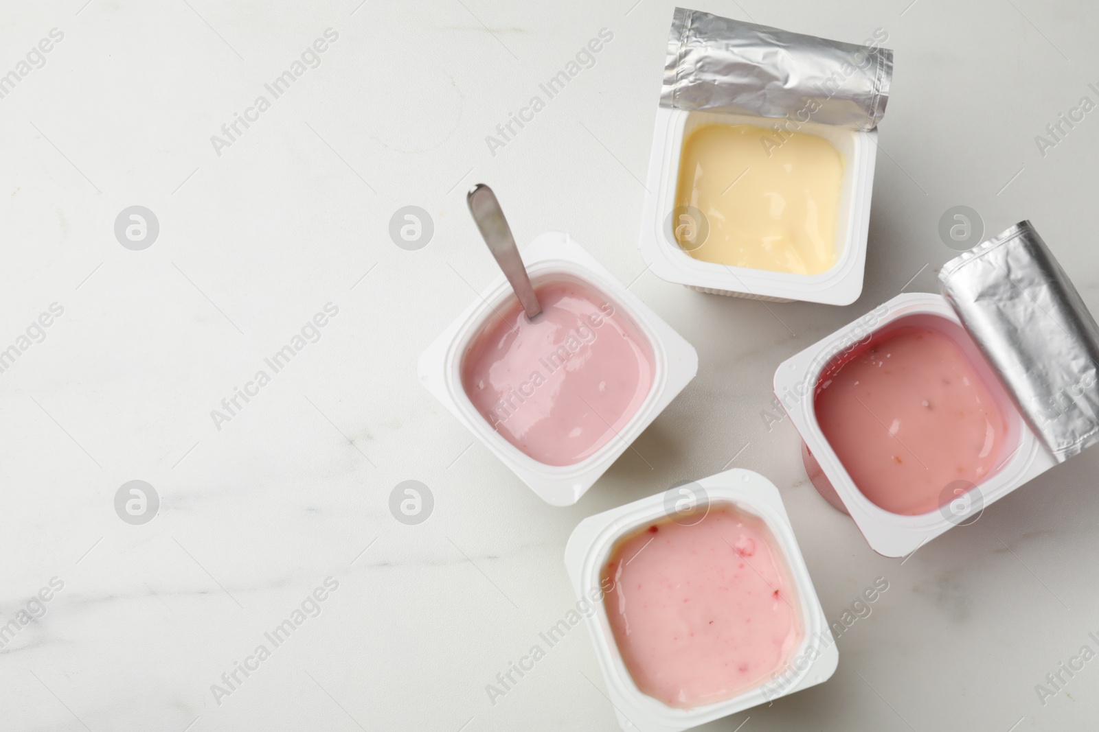 Photo of Delicious yogurts in plastic cups on white marble table, flat lay. Space for text