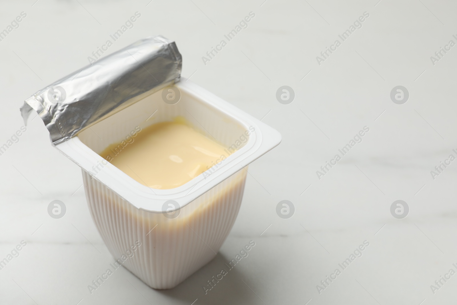 Photo of Delicious yogurt in plastic cup on white marble table, closeup. Space for text