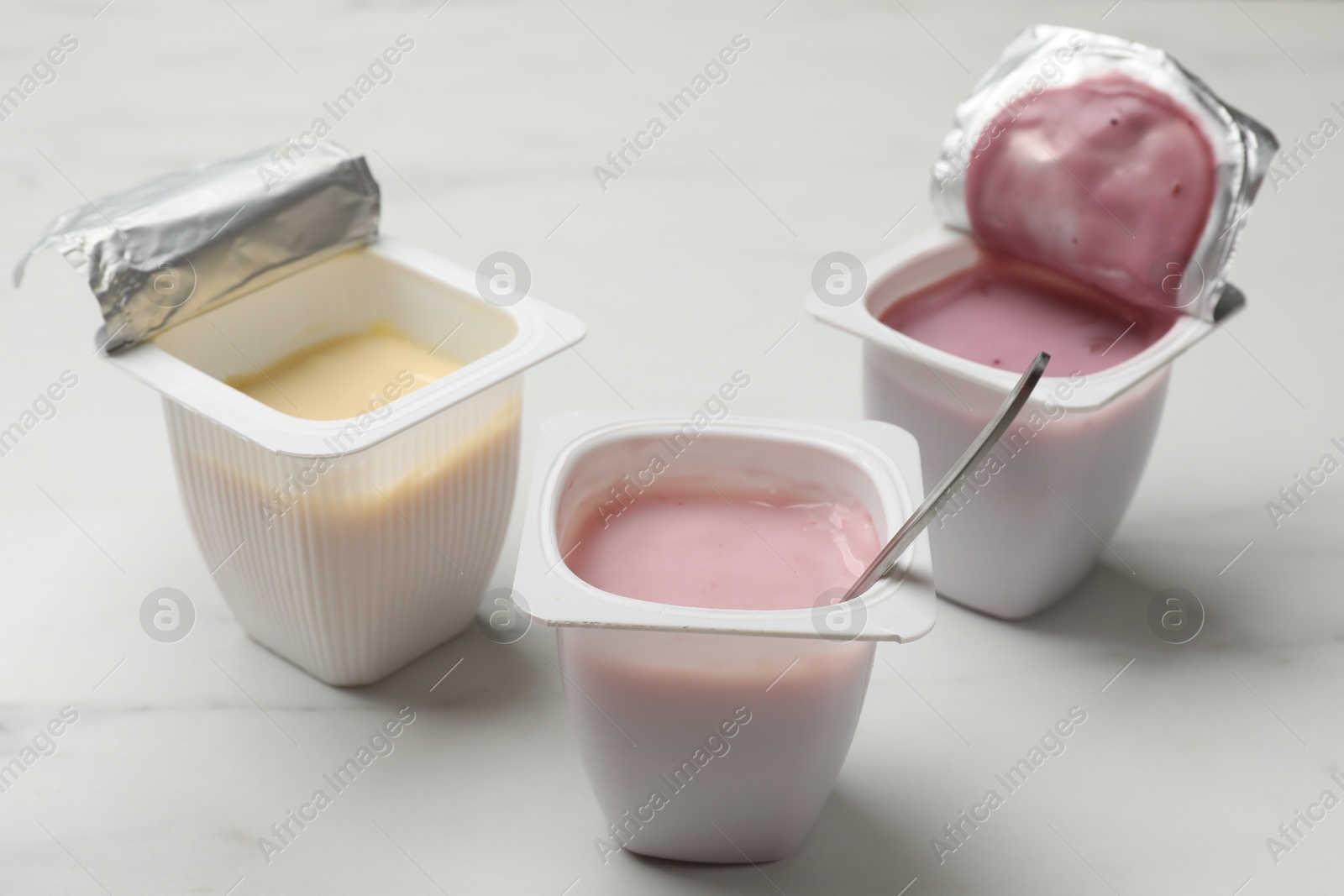 Photo of Delicious yogurts in plastic cups on white marble table, closeup