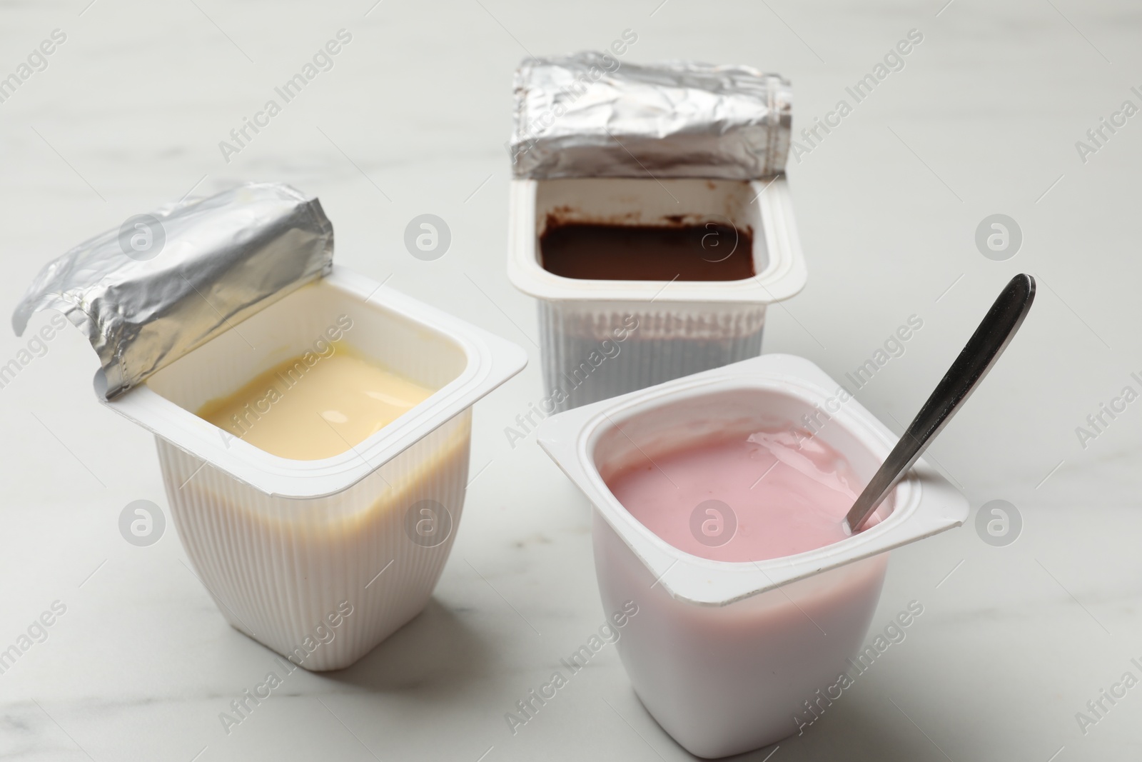 Photo of Delicious yogurts in plastic cups on white marble table, closeup