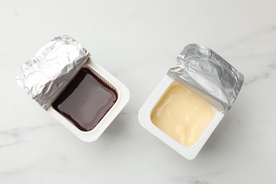 Photo of Delicious yogurts in plastic cups on white marble table, flat lay