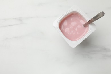 Photo of Delicious yogurt in plastic cup with spoon on white marble table, top view. Space for text