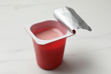 Photo of Delicious yogurt in plastic cup on white marble table, closeup